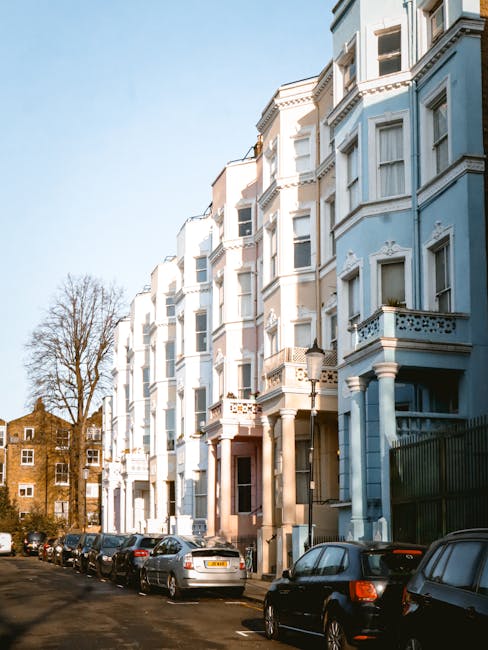 A row of pastel-colored Victorian-style residential buildings in Notting Hill, featuring various shades of purple, yellow, blue, and pink. Each building has large, multi-pane sash windows with white f